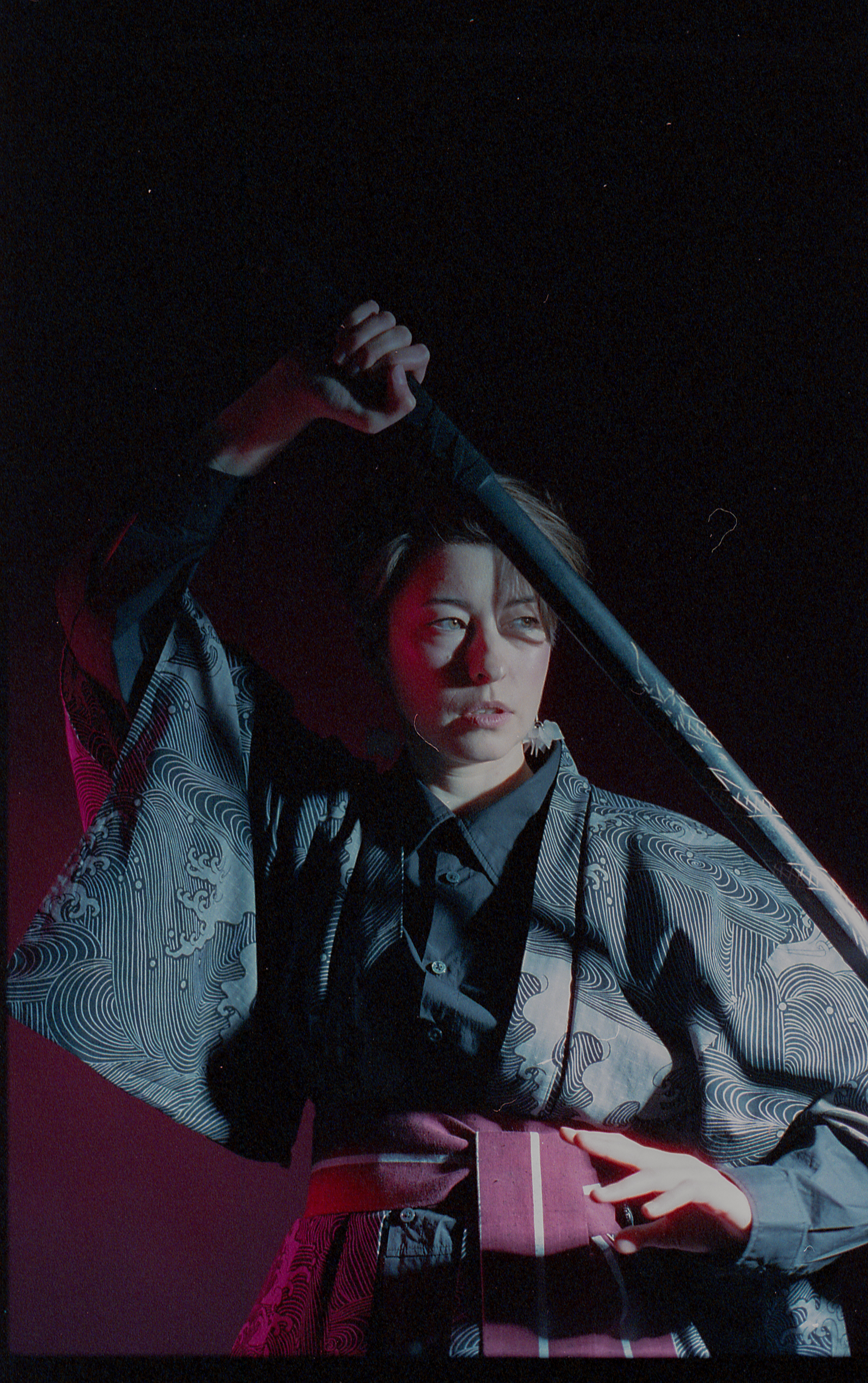 Yulia lowering the blade, lit in blue and crimson